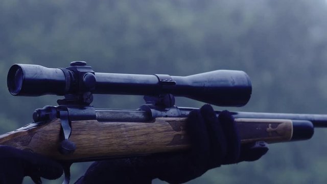 Close up side view of a person holding a rifle with mounted telescopic sight, 30 fps.