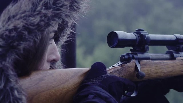 Close up side profile of a woman holding still while aiming a rifle at night, 30 fps.