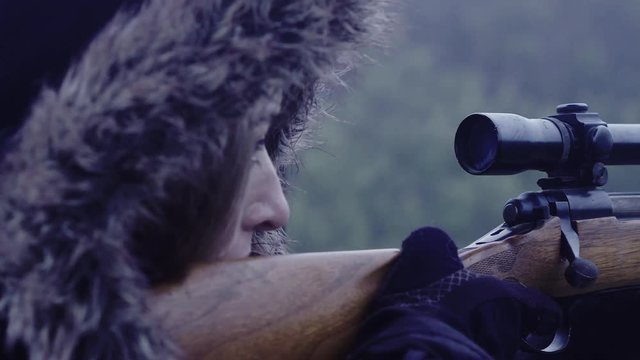 Close up side profile of a female hunter holding still while aiming a rifle, 30 fps.