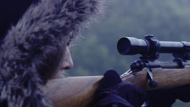 Close up side profile of a female hunter holding a rifle steady while aiming, 30 fps.