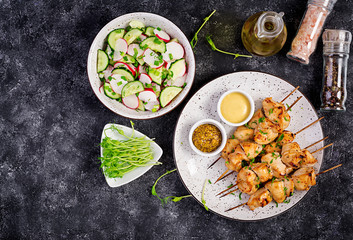 Grilled chicken kebab and salad with cucumber, radish, onion on a dark background. Copy space. Top view