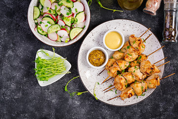 Grilled chicken kebab and salad with cucumber, radish, onion on a dark background. Copy space. Top view
