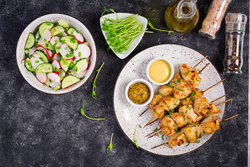 Grilled chicken kebab and salad with cucumber, radish, onion on a dark background. Copy space. Top view