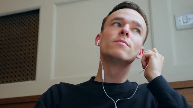 Young man taking off white earphones and touching his face