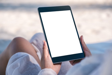 Mockup image of a woman holding a black tablet pc with blank desktop screen while laying down on...