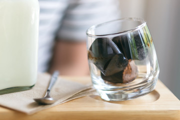 A glass of ice cube coffee and a bottle of milk on wooden saucer