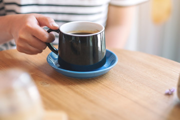 Closeup image of a woman's hand holding a green cup of hot coffee on wooden table