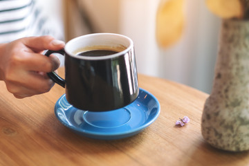 Closeup image of a woman's hand holding a green cup of hot coffee on wooden table