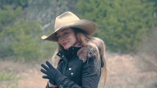 A cowgirl adjusts her gloves into her jacket while standing outside in the cold on the farm.