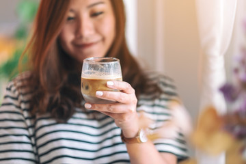 Closeup image of a beautiful woman holding a glass of iced coffee to drink in cafe