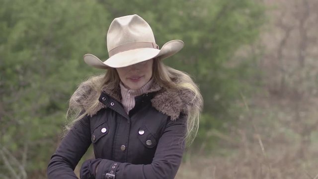 A cowgirl with face hidden under a hat, adjusts her winter gloves out on the farm.