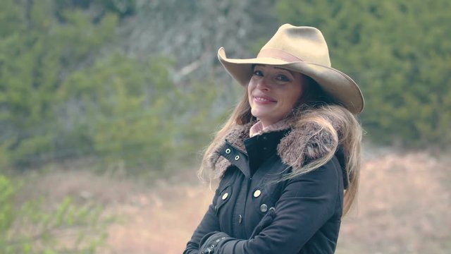 A happy looking cowgirl dressed for winter, standing to the side of frame, 29.97 fps.