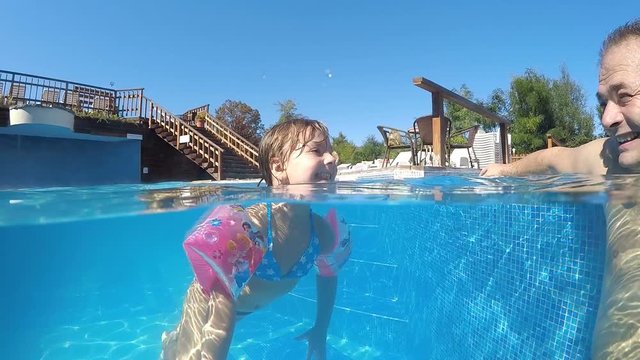 Little funny girl having fun refreshing in thermal pool with father. She takes tongue out of mouth, SLOW MOTION