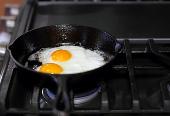 Two eggs frying sunny-side up in a cast iron pan on the stove.