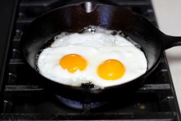 Two eggs frying sunny-side up in a cast iron pan on the stove.