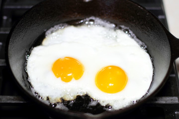 Two eggs frying sunny-side up in a cast iron pan on the stove.