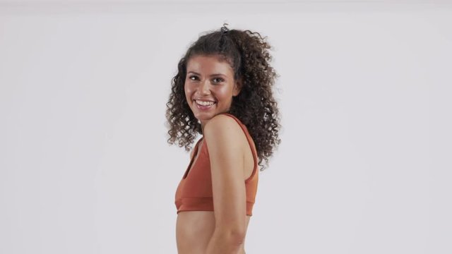 Caucasian girl plays with her curly, long, brown hair, enjoying herself while posing during a video and photo shoot.