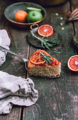 citrus upside down cake with blood oranges, lemons and limes on wooden board among fresh citrus fruit, kitchen stuff, herbs and spices on old wooden background, toned for a vintage effect