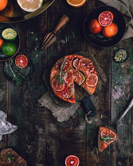 citrus upside down cake with blood oranges, lemons and limes on wooden board among fresh citrus fruit, kitchen stuff, herbs and spices on old wooden background, toned for a vintage effect