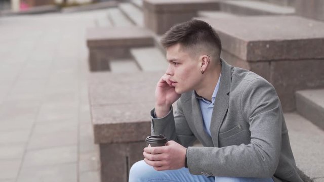 Young man sitting outdoor having coffee and  talking over mobile phone.