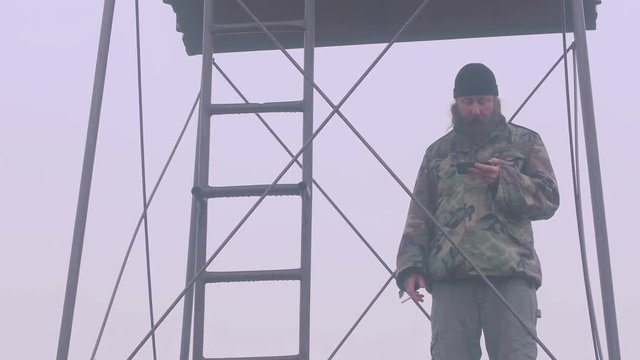 Man standing on guard tower outpost smoking looking at smartphone