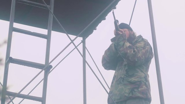 Dangerous man standing in tower with gun, looking through scope at targets