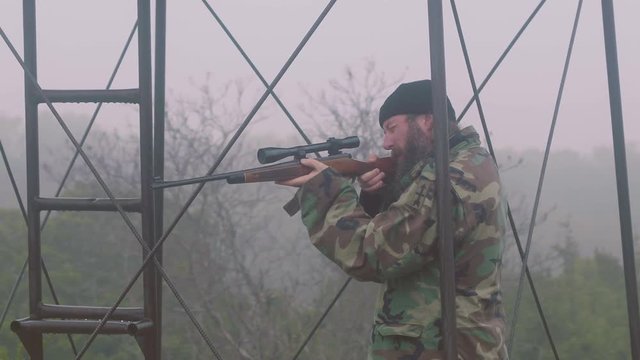 Guerrilla fighter standing guard in outpost, gun ready, looking through scope then lowering