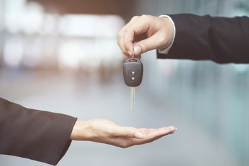 Car key, businessman handing over gives the car key to the other woman on showroom background.