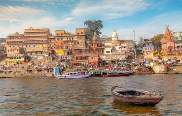 Ancient Varanasi city architecture with view of a wooden boat on river Ganges at sunset