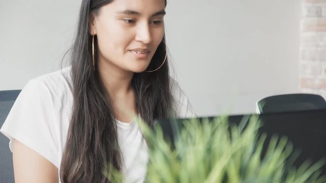 A happy young woman looking at a computer screen at her office, focused on her task. Medium close-up shot, slow motion.