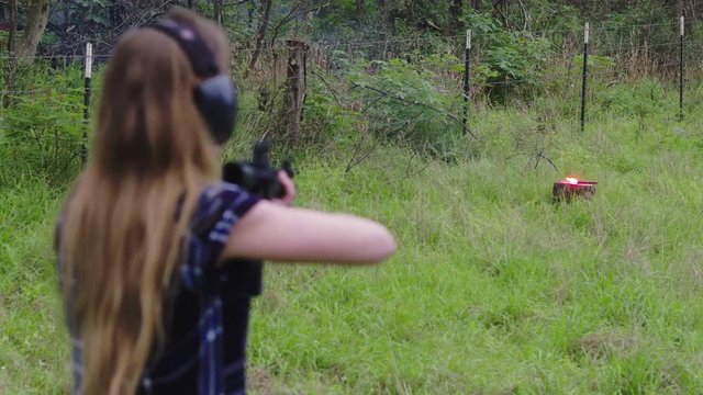 View behind a woman aiming and missing the explosive target during shooting practice, slow motion 24fps.