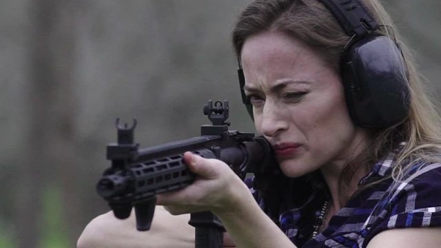 Close up view in front of a woman getting kickback from firing a weapon multiple times at a target, slow motion 24 fps.