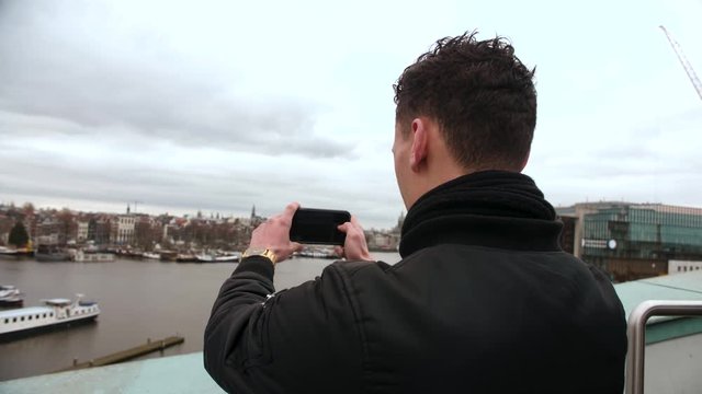 Male tourist takes photos from the skyline of Amsterdam with his mobile phone