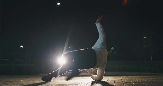 Slow motion of young break dancer is having fun to dancing with car lights at city parking at night.