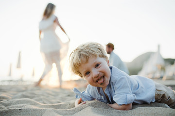 A small toddler boy standing on beach on summer holiday, having fun.