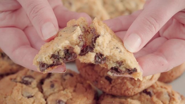 Hands breaking half fresh chocolate chip cookie into quarters, Slowmo Close Up