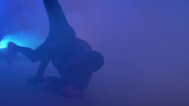 Slow motion shot of African youth doing impressive bread dancing spins on his back in colorful smoke.