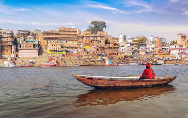 Sadhu on a wooden boat on river Ganges with view of ancient Varanasi city architecture at sunset