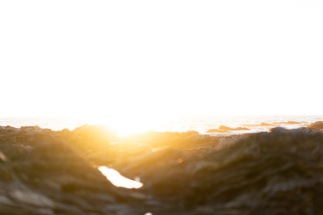 White sky during sunset with optical flare on black rocky beach