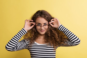 Naklejka premium Portrait of a young woman with glasses in a studio on a yellow background.