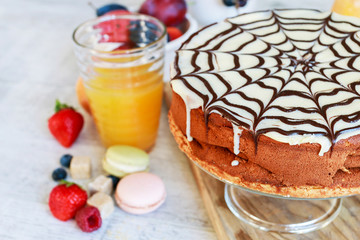 Halloween chocolate spider web cake and various fruits around.