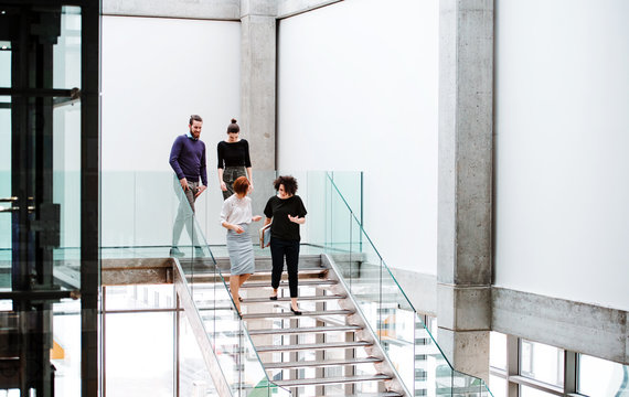 Group Of Young Businesspeople Walking Down The Stairs, Talking.