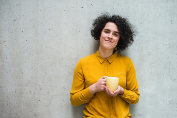 A portrait of young businesswoman standing in office, holding a cup of coffee.