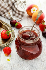 Jar of strawberry jam among summer and autumn fruits