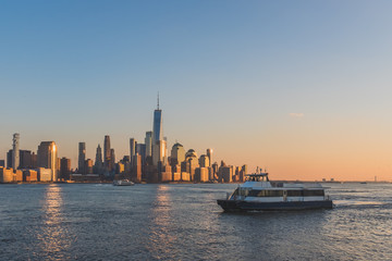 Fototapeta na wymiar Boats traveling on Hudson River with skyline of lower Manhattan at sunset