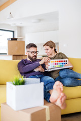 A young couple with color samples sitting on sofa, moving in new home.
