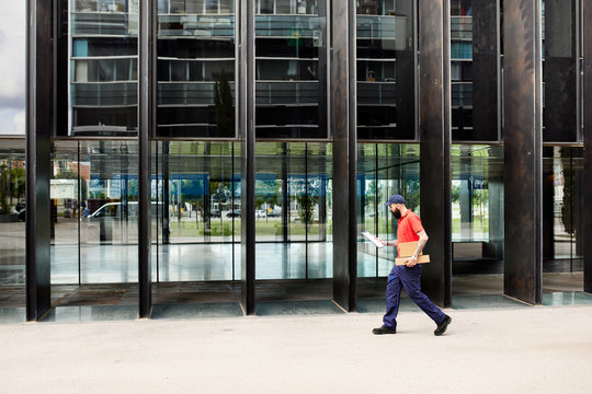 Courier walking with parcel and clipboard.