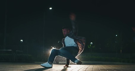 Slow motion of young break dancer is having fun to dancing with car lights at city parking at night.