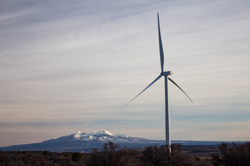A wind turbine at a high elevation prairie landscape with mountains on the horizon.