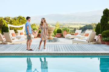 Couple standing by pool at luxury resort talking and looking at each other